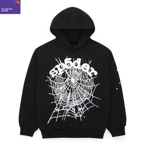 以下が含まれることがあります： 白いクモの巣のグラフィックと「sp5der」の文字が入った黒いフード付きスウェットシャツ。スウェットシャツにはフロントポケットとフードが付いています。袖には小さな星のデザインがあります。