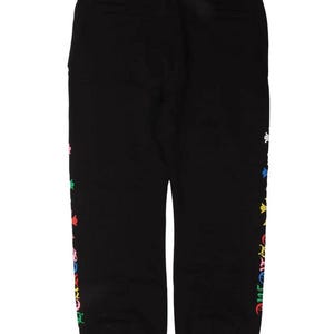 Op de afbeelding: Zwarte joggingbroek met een kleurrijk bloemenpatroon aan de zijkant. De broek heeft een elastische tailleband en een klein logo bij de enkel. De tekst "Trend On Earth" staat in de linkerbovenhoek.