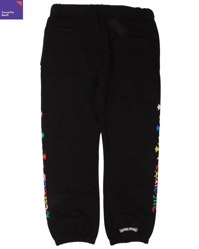 Op de afbeelding: Zwarte joggingbroek met een kleurrijk bloemenpatroon aan de zijkant. De broek heeft een elastische tailleband en een klein logo bij de enkel. De tekst "Trend On Earth" staat in de linkerbovenhoek.