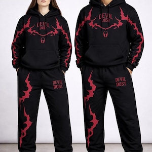 May include: Black hoodie and sweatpants set with red graphic designs. The hoodie features "DEVIL DUST" text and a stylized design across the chest and sleeves. The sweatpants have matching graphics. The set is worn by two people.