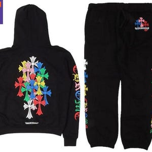 Pode incluir: Conjunto de moletom com capuz e calças de moletom pretas. O moletom com capuz apresenta um design de cruz colorida nas costas e a palavra "Chrome Hearts" na parte inferior. As calças de moletom têm um design de cruz correspondente.