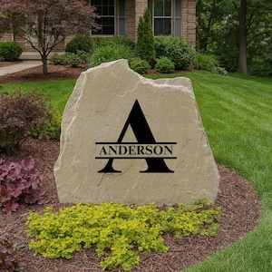 May include: A large, natural stone sign with the name "Anderson" and the letter "A" in black. The sign is set in a landscaped yard with green grass, mulch, and colorful plants. The house is visible in the background.