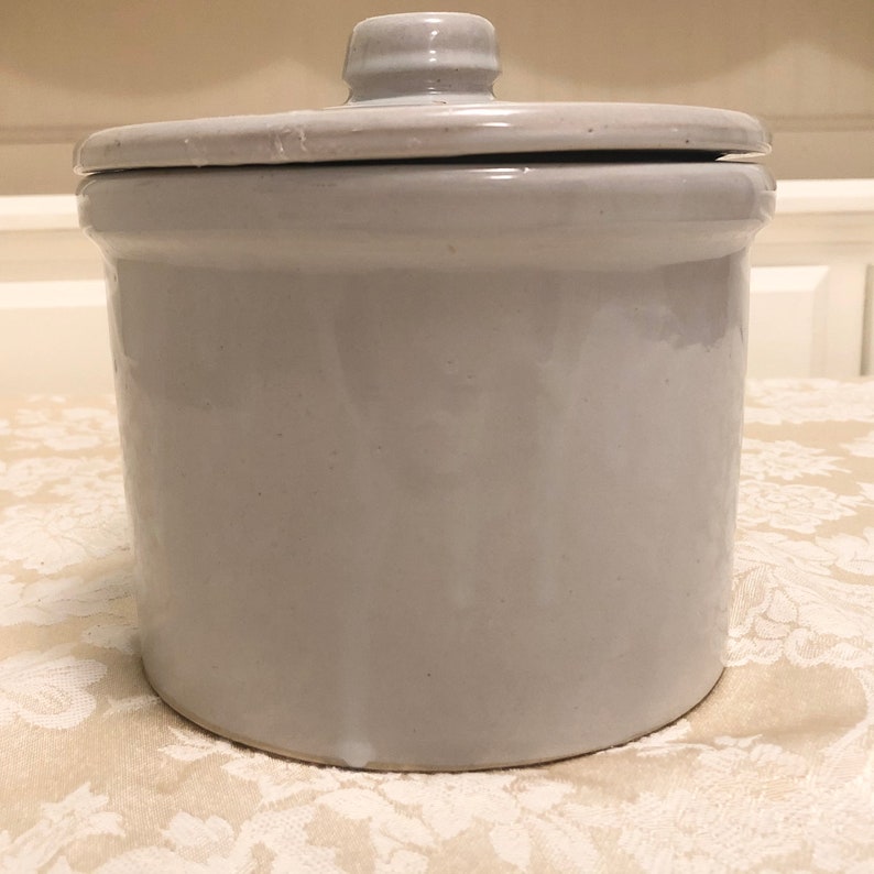 May include: A white ceramic crock with a lid. The crock is glazed and has a smooth finish.
