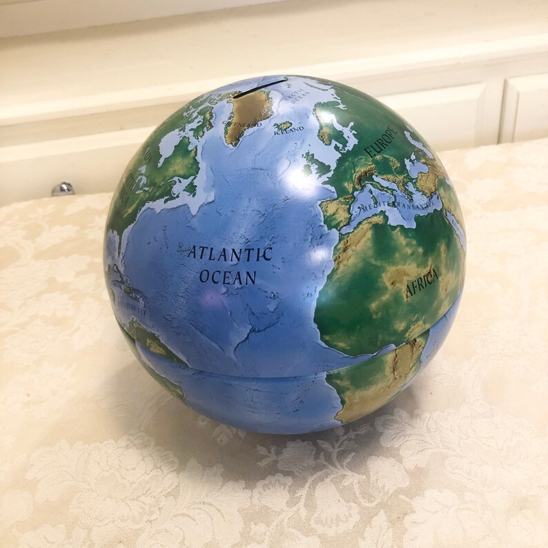 May include: A blue and green globe piggy bank with a slot on the top. The globe shows the continents of North America, South America, Europe, Africa, Asia, and Australia. The words "Atlantic Ocean" are printed on the globe.