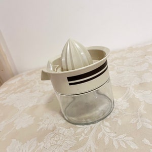 May include: White plastic citrus juicer with a black stripe design. The juicer has a clear glass base and a removable white plastic cone.