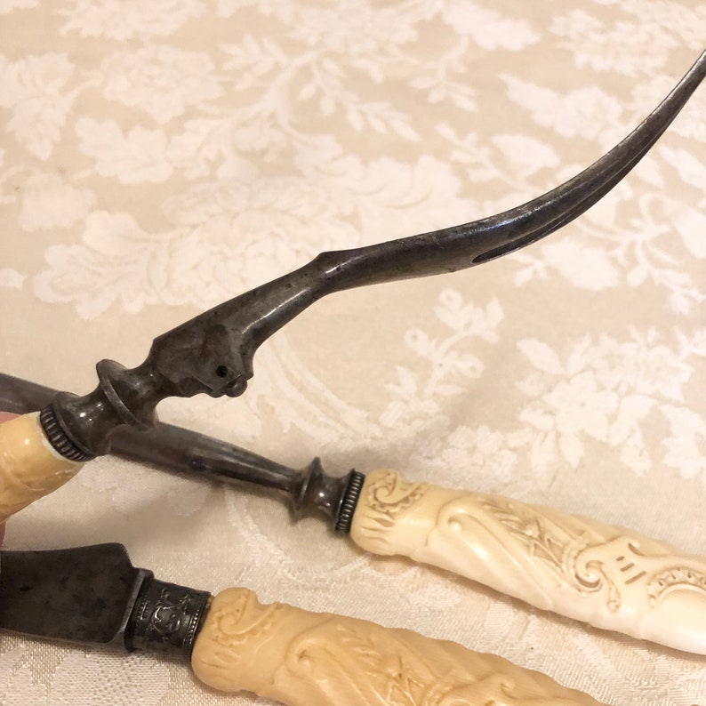 May include: A set of three antique silver serving utensils with carved ivory handles. The utensils have ornate designs and are in excellent condition.