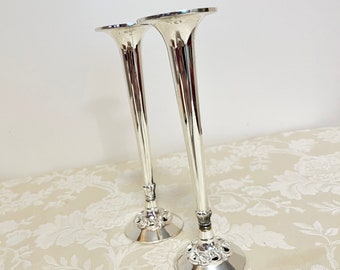 May include: A pair of silver plated trumpet shaped bud vases. The vases have a decorative base with a floral design.