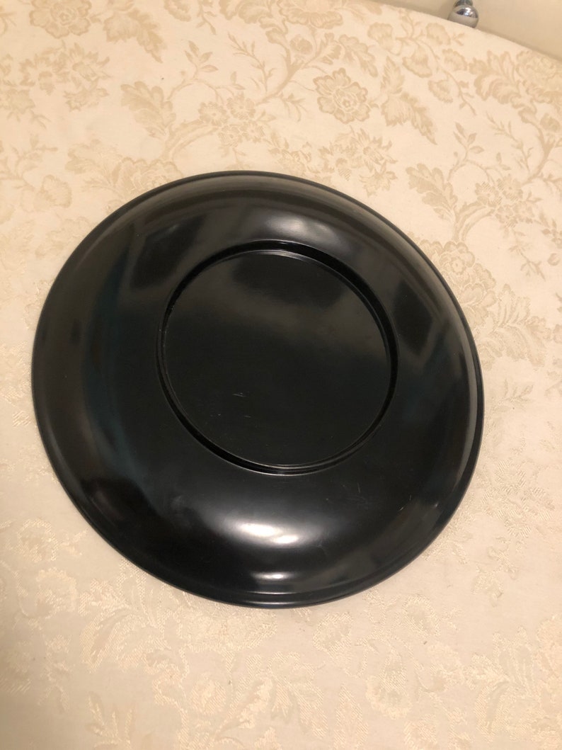 May include: A black lacquer tray with a raised rim and a smooth, glossy finish. The tray is circular and has a smaller, circular inset in the center.