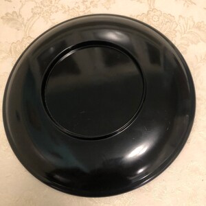 May include: A black lacquer plate with a raised rim and a smaller, concentric circle in the center.