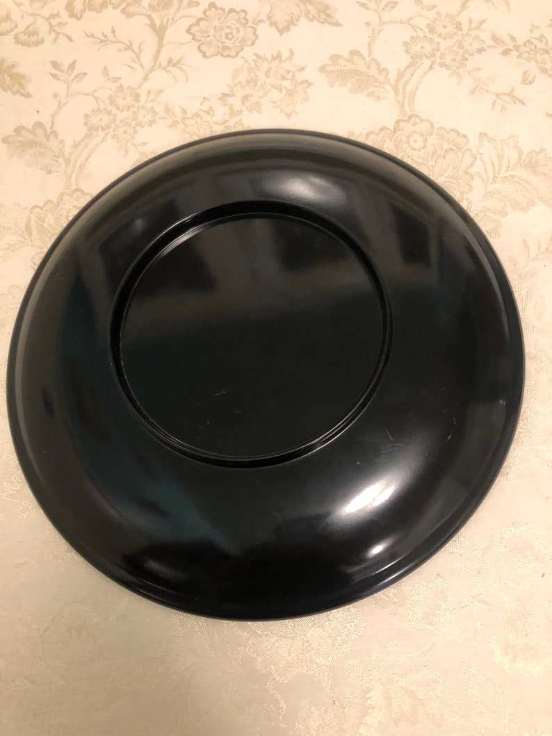 May include: A black lacquer plate with a raised rim and a smaller, concentric circle in the center.