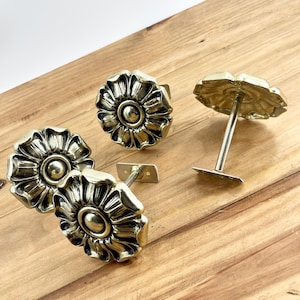 May include: Four gold metal curtain holdbacks with a floral design. Each holdback has a decorative finial in the shape of a flower with a center circle.