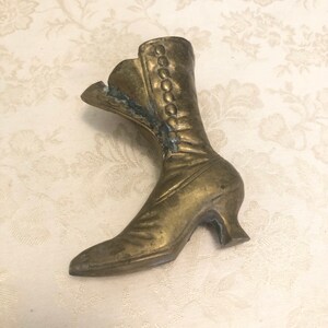May include: A vintage brass boot figurine. The boot is detailed with a lace-up design and a high heel.