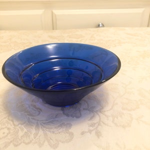 May include: A cobalt blue glass bowl with a fluted rim. The bowl is empty and sitting on a white tablecloth with a floral pattern.