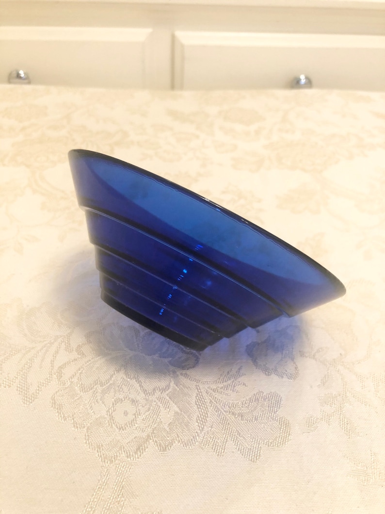 May include: A cobalt blue glass bowl with a fluted design. The bowl is made of thick glass and has a rounded shape.