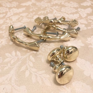May include: A set of six gold-toned cabinet knobs and pulls. The knobs are round and the pulls are shaped like a curved handle with a decorative fan-shaped end.