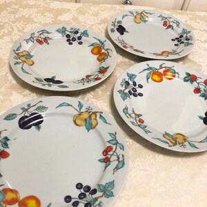 May include: Set of four white ceramic dinner plates with a fruit design. The plates feature a border of pears, plums, berries, and leaves in shades of green, yellow, orange, red, and purple.