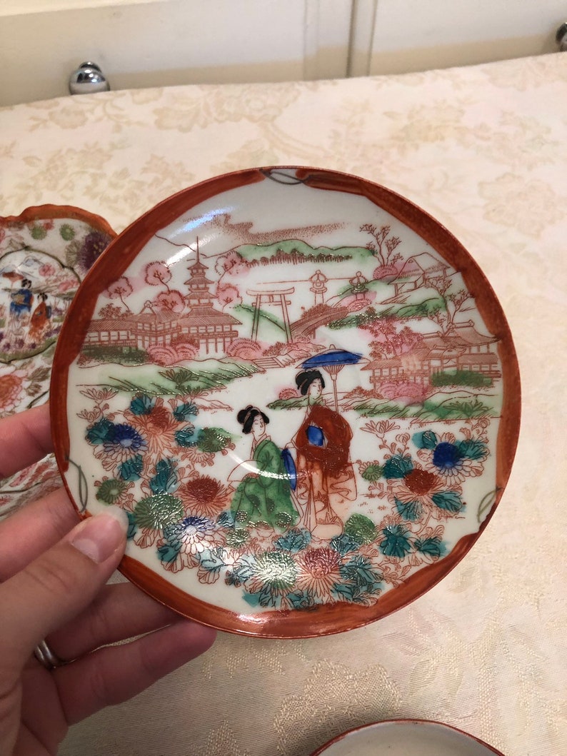 Antique Rose Medallion Chinese Lotus Nut Bowl And Tea Cups And Saucers Detailed In Gold And Red Trim Framing The Elegant Garden With Ladies