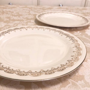 May include: Two white ceramic plates with gold trim and a delicate floral pattern. The plates are on a white tablecloth.