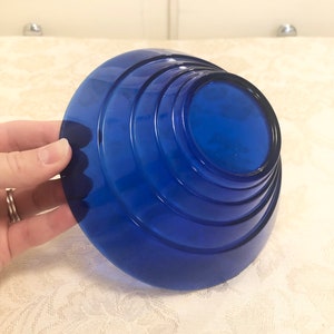 May include: A cobalt blue glass bowl with a layered, stepped design. The bowl is round and has a wide, flat base.