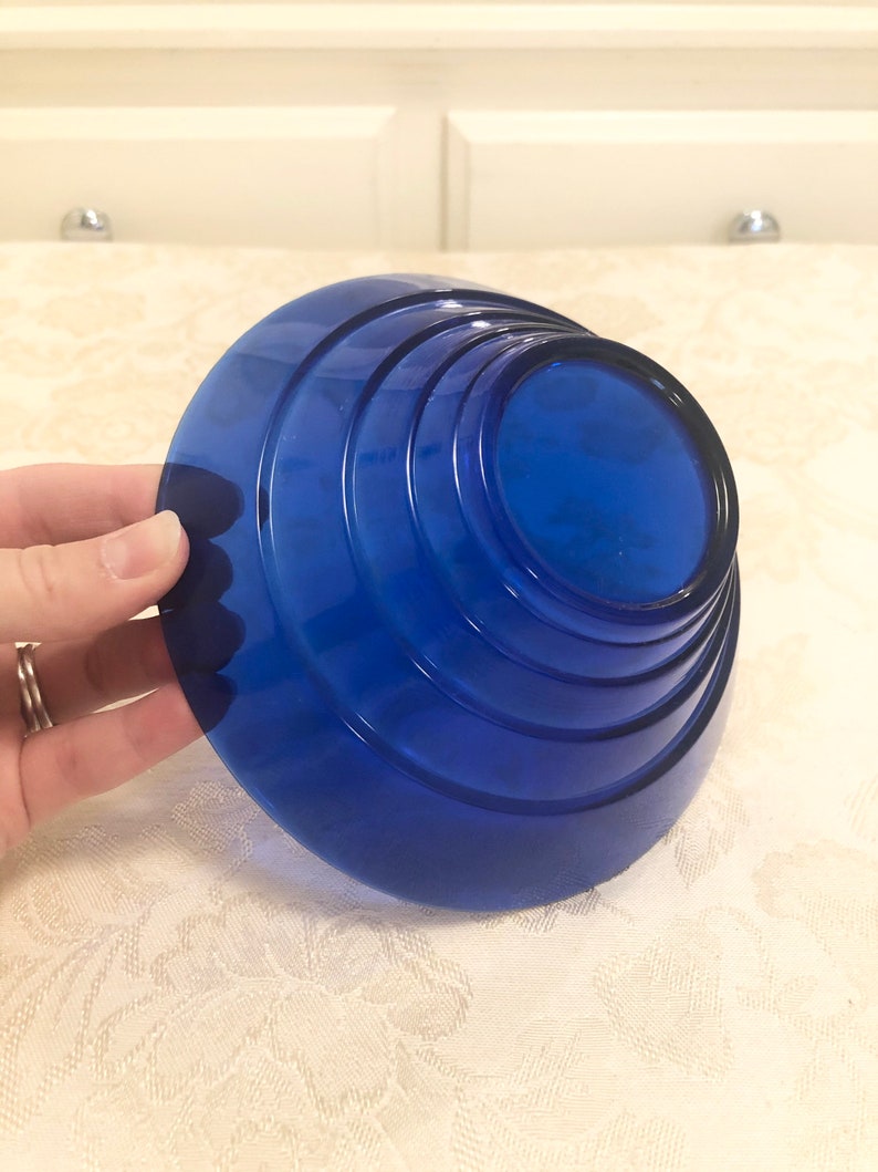 May include: A cobalt blue glass bowl with a layered, stepped design. The bowl is round and has a wide, flat base.