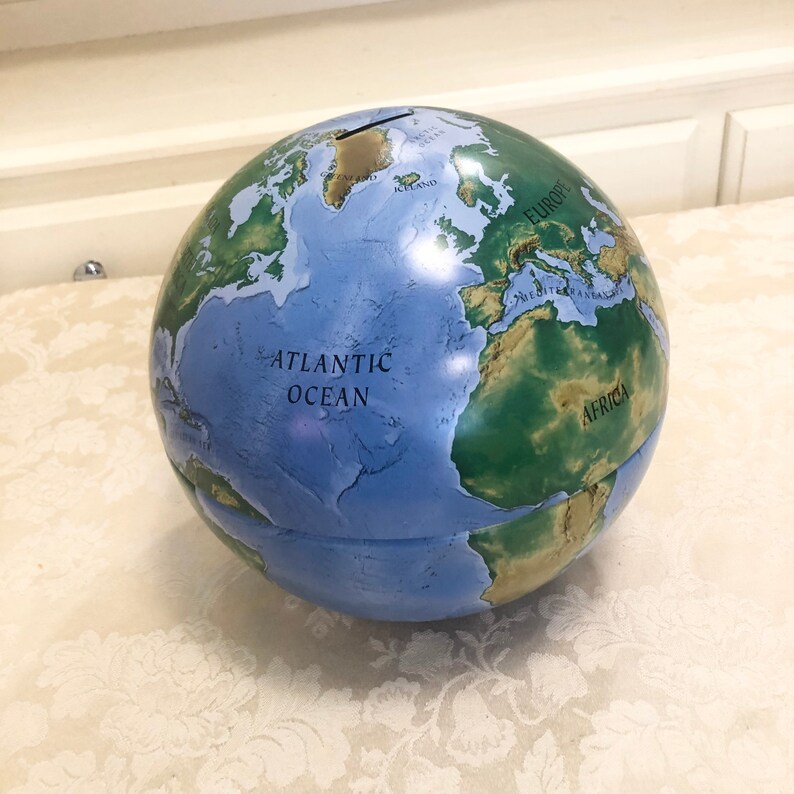 May include: A blue and green globe piggy bank with a slot on the top. The globe has a map of the world with the continents labeled in black text. The text "ATLANTIC OCEAN" is visible on the globe.