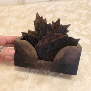 May include: A set of six wooden coasters in the shape of leaves, with a carved design. The coasters are in a wooden holder with a dark brown finish.