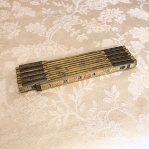 May include: A vintage wooden folding ruler with a brass extension mechanism. The ruler is marked in inches and has a red "JUNK" label. The ruler is 7 inches long when fully extended.