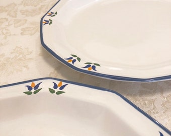 May include: Two white ceramic serving platters with a blue border and floral accents. The platters have an octagonal shape. The floral accents are in shades of blue, yellow, and green.