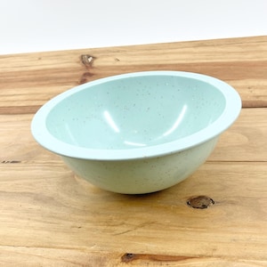 May include: A light blue speckled bowl with a rounded shape. The bowl is made of a solid material and has a smooth, glossy finish. The bowl is sitting on a wooden surface.