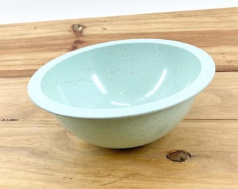 May include: A light blue speckled bowl with a rounded shape. The bowl is made of a solid material and has a smooth, glossy finish. The bowl is sitting on a wooden surface.