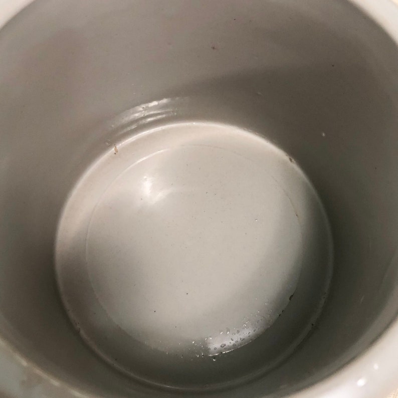May include: The inside of a white ceramic crock pot. The interior is smooth and white.