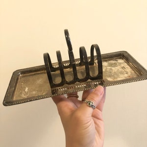 May include: Silver plated bread rack with a decorative border. The rack has four slots for holding bread.