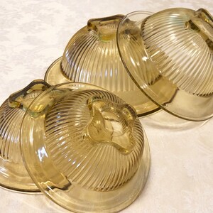 May include: Three vintage glass mixing bowls with a ribbed design. The bowls are a pale yellow color and are stacked on top of each other.