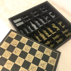 May include: A black and gold chess set with a cracked board and metal pieces. The pieces are stored in a black box with a velvet lining.