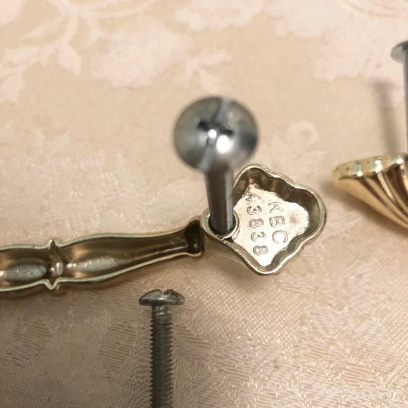 Puede incluir: Herraje de armario dorado con un dise&ntilde;o decorativo. La parte posterior de la manija tiene el texto "KBC 43838" grabado.