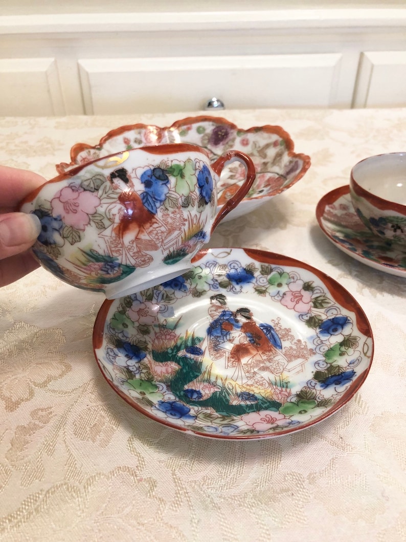 Antique Rose Medallion Chinese Lotus Nut Bowl And Tea Cups And Saucers Detailed In Gold And Red Trim Framing The Elegant Garden With Ladies