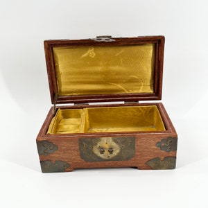 May include: A wooden jewelry box with brass accents and a gold velvet interior. The box has a hinged lid and a compartment for storing jewelry.