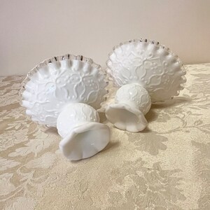 May include: Two white milk glass candle holders with a silver trim and a floral design.
