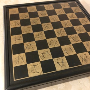 May include: A black and gold chessboard with a distressed finish. The board is framed in black wood.