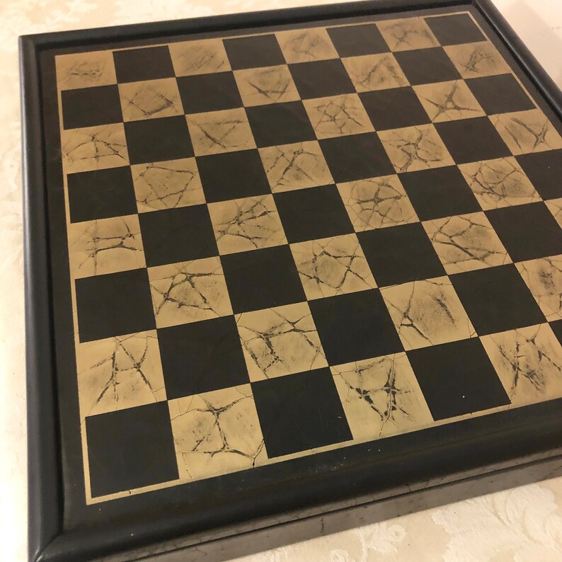 May include: A black and gold chessboard with a distressed finish. The board is framed in black wood.