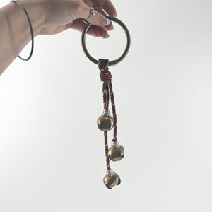 May include: A brass ring with a red, green, and gold rope attached. Three brass bells hang from the rope.
