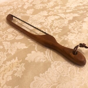 May include: A wooden handled bread knife with a serrated blade and a leather loop at the end of the handle.