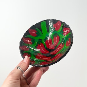 May include: A small black bowl with a red and green chili pepper design. The bowl is made of paper mache and is perfect for serving snacks or dips.