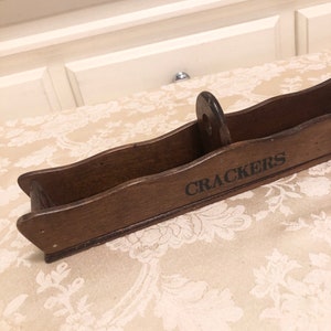 May include: A wooden cracker box with a handle and the word "CRACKERS" printed on the front.