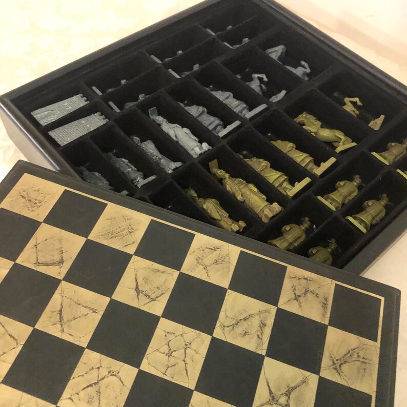 May include: A black and gold chess set with a wooden board and metal chess pieces. The board has a distressed look with a cracked finish. The pieces are arranged in their starting positions.