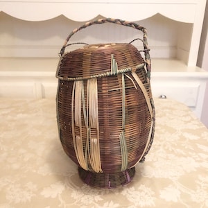 May include: A woven brown, green, and purple basket with a handle. The basket has a round base and a rounded top.