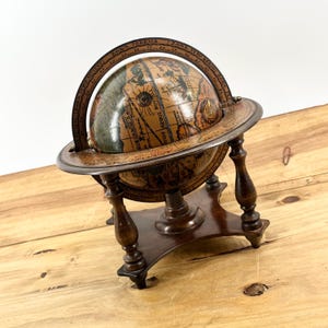 May include: A vintage-style globe with a detailed map design, mounted on a dark wooden stand. The globe features a brass meridian ring and sits on a base with four decorative legs. The globe is a decorative item.
