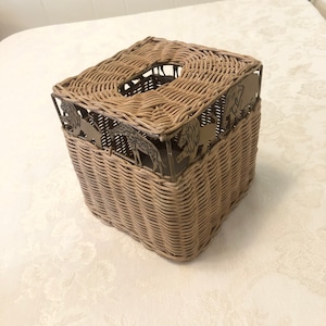 May include: A woven wicker tissue box cover with a metal frame featuring cut-out animal silhouettes. The animals include an elephant, giraffe, and lion.
