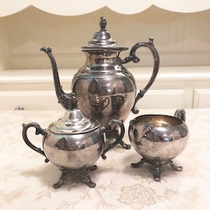 May include: A silver tea set with a teapot, creamer, and sugar bowl. The set has a traditional design with ornate details and a polished finish.
