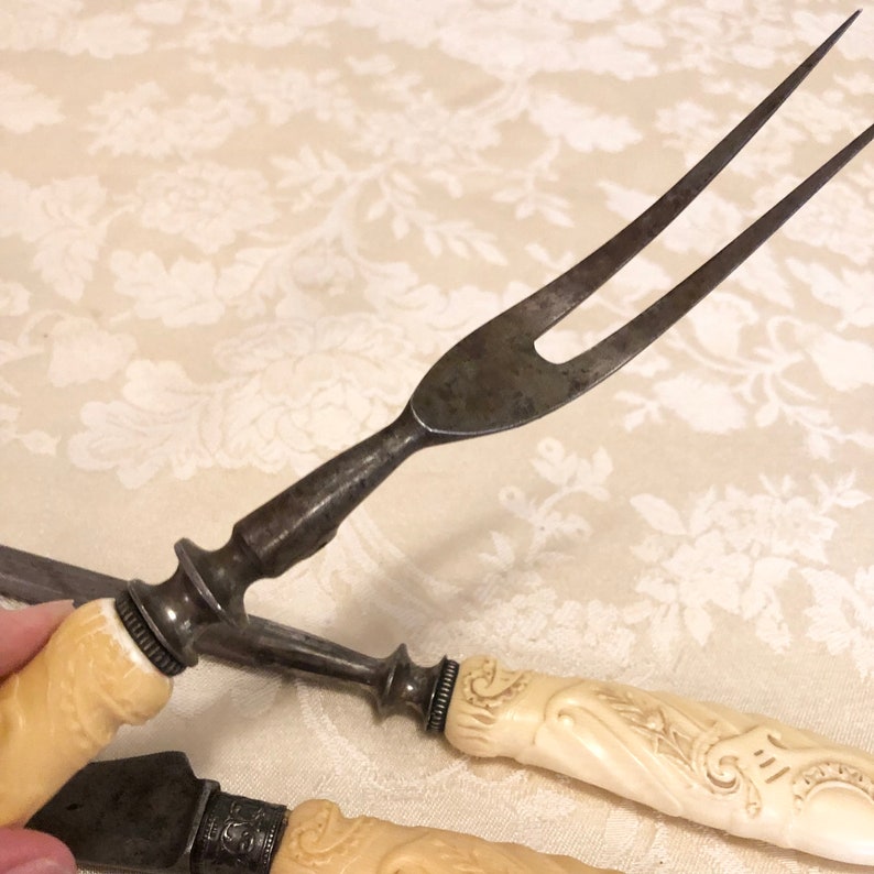 May include: A set of two antique carving knives with ivory handles. The knives have ornate designs on the handles and are in good condition.